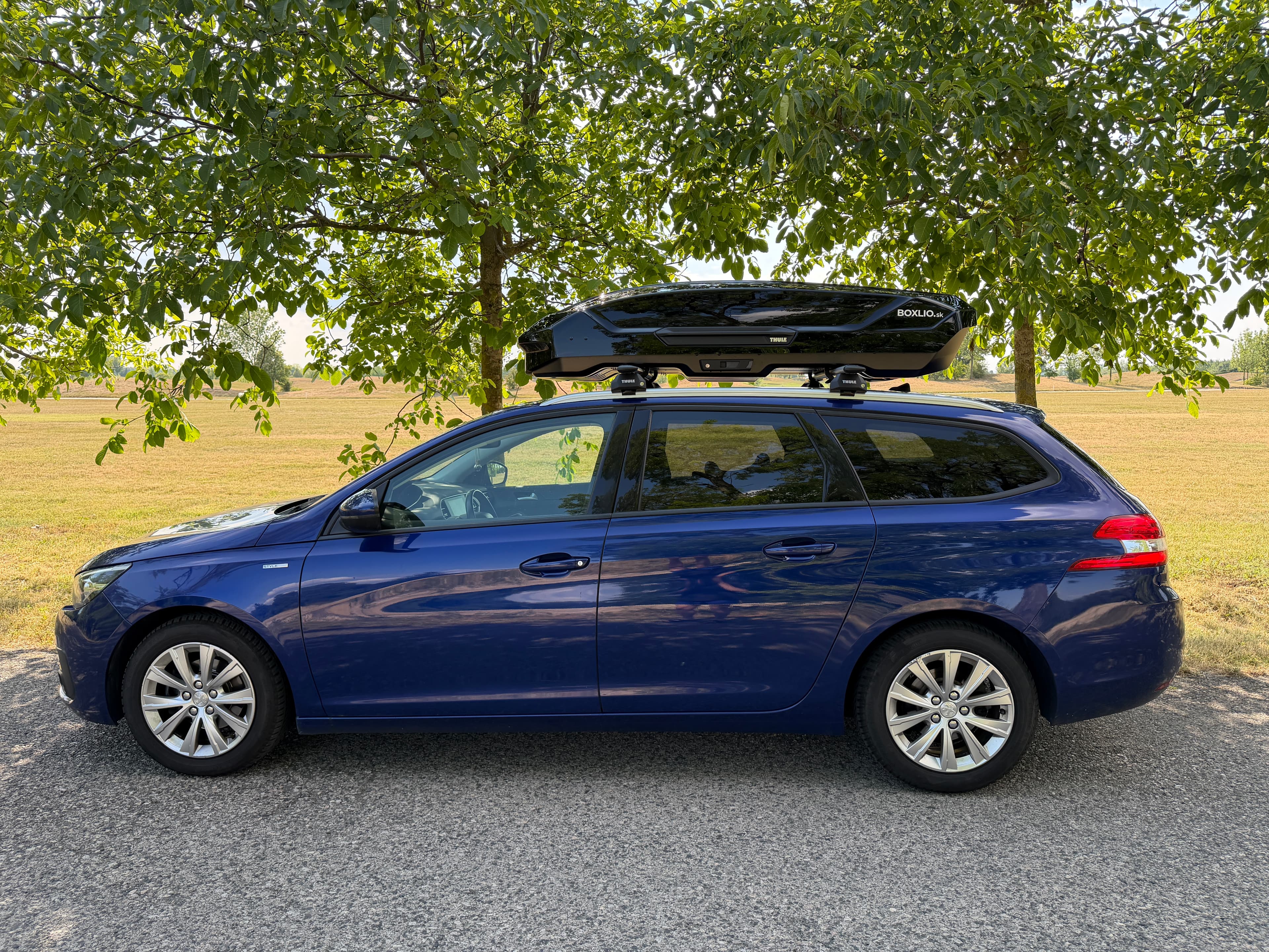 Modré auto Peugeot so strešným boxom THULE BOXLIO zaparkované na prírode